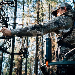 Bow hunter in a tree stand and a locking cup holder attached to the bar. The cup holder has an insulated canteen secured in it.