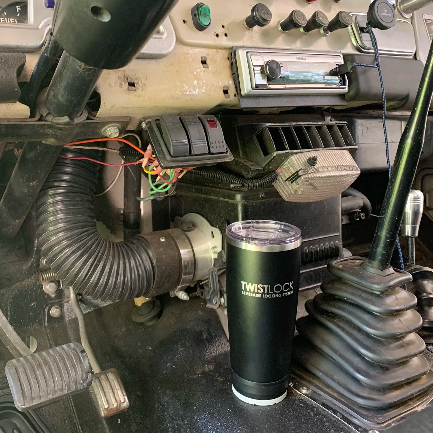 Low profile mini disc locking cup holder on the floor of an old truck with a tumbler in it.