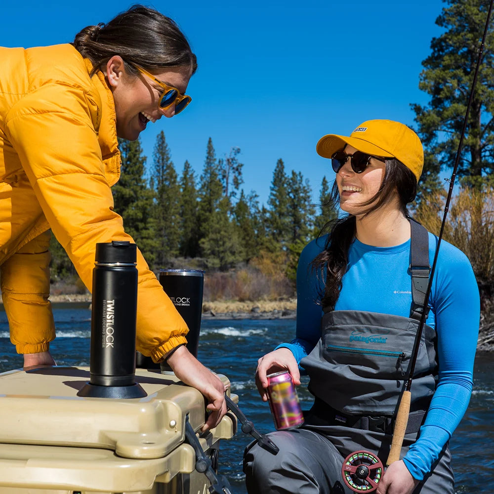 Two fishers at the river with an insulated tumbler and canteen attached to the cooler lid.